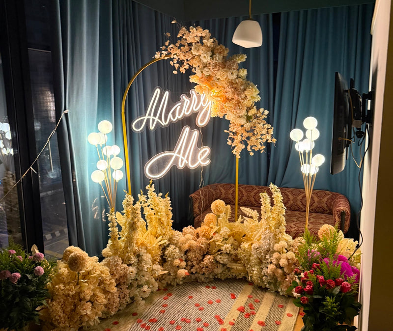 Marry Me proposal backdrop with gold floral arch, neon sign and seating corner